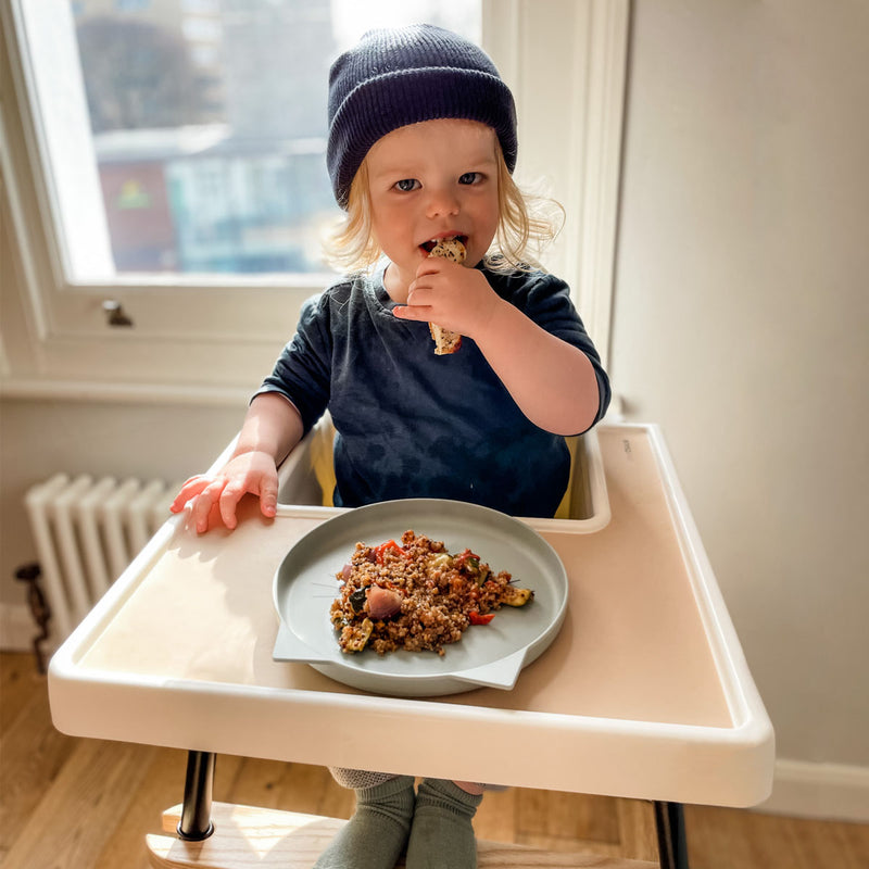 toddler wearing hat enjoying lunch using ikea high chair with cream placemat